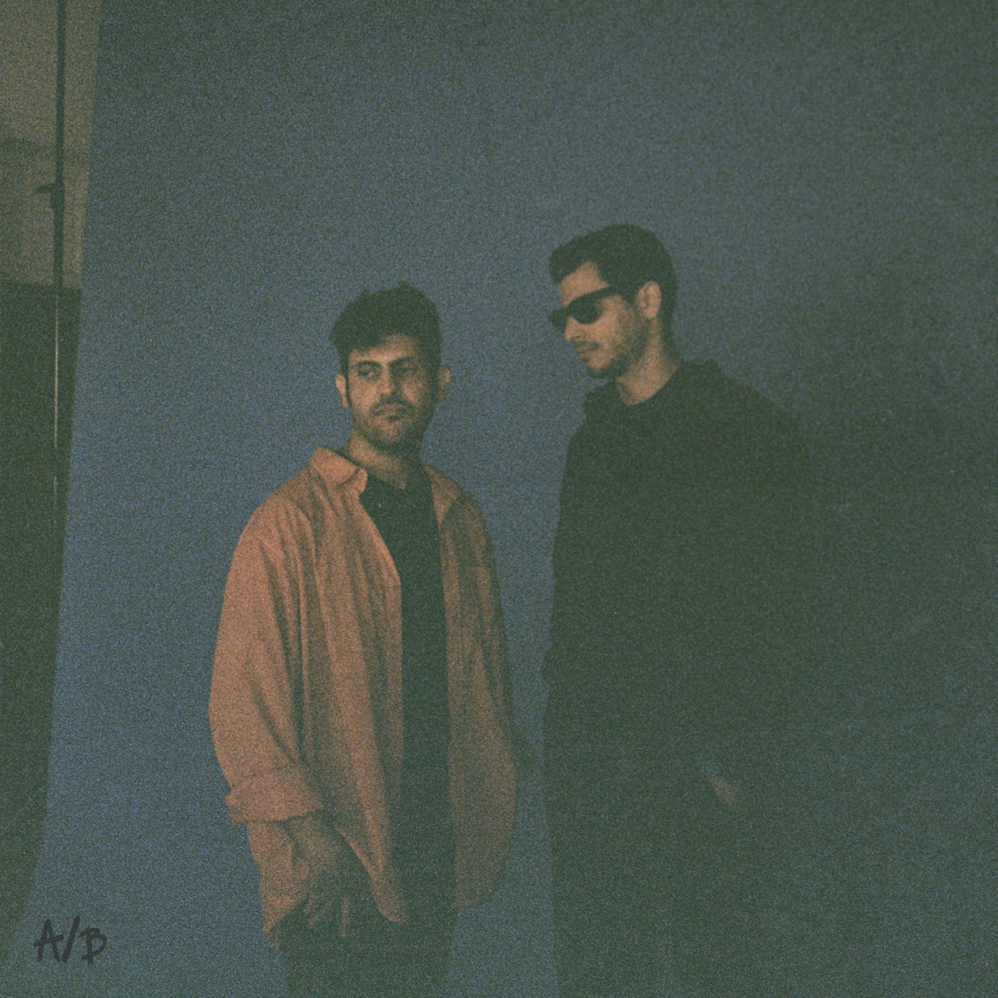 The two members of A/B standing against a blue wall